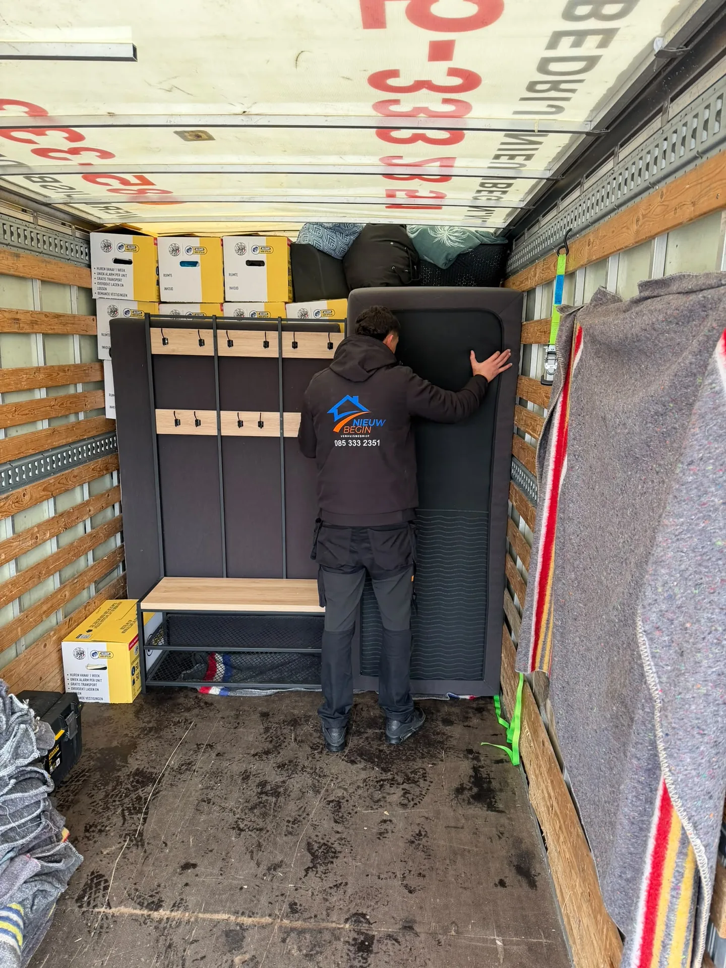 Verhuizer van Nieuw Begin zet een kast vast in de wagen met verhuisdekens