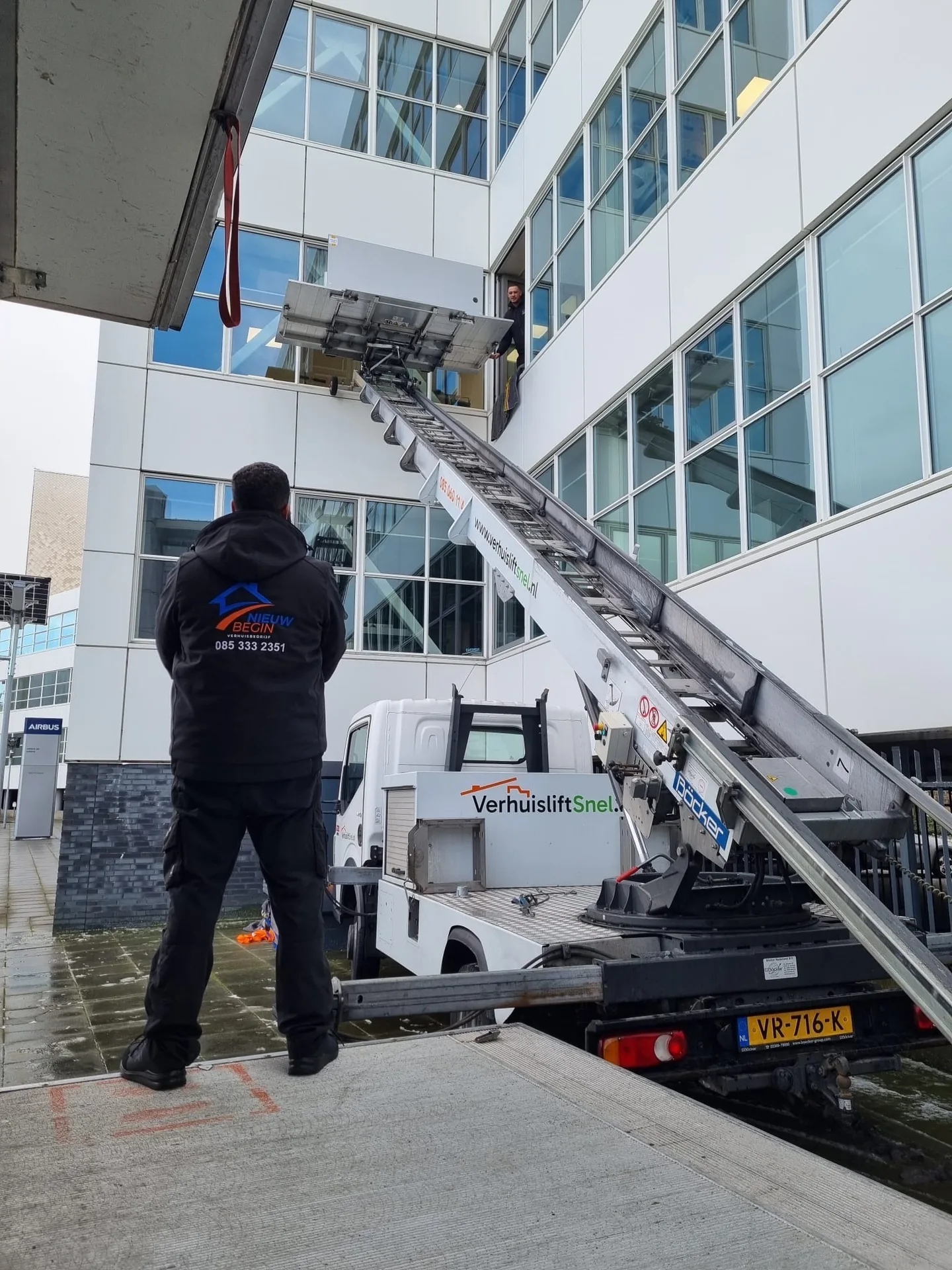 Verhuizer van Nieuw Begin bij de verhuislift tegen een kantoorpand met glazen gevel